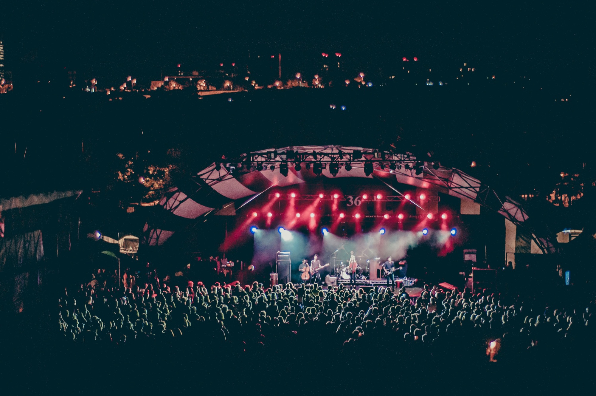 A concert stage in red light seen across a large crowd